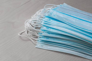 Mavi renkli tek kullanımlık tıbbi maskeler gri bir masanın üzerinde yan yana yatar..