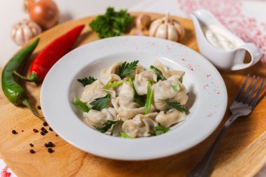 Beyaz bir tabakta ev yapımı hamur köftesi ve tahta bir tahtanın üzerinde otlar.