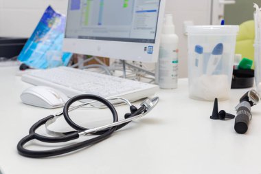 Tıp bürosu. Doktorun ofisinde beyaz bir masa. Bilgisayarın arka planında steteskop var..