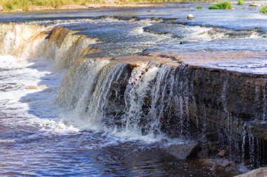 Tosno Nehri 'nin yakınındaki şelalede. Güneşli bir yaz gününde dalgalı bir nehir ve kayalık bir sahil. Sablino, Leningrad bölgesi, Rusya