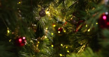 Kamera, parlak toplar ve ışıklarla süslenmiş Noel ağacının dalları arasında hareket eder.