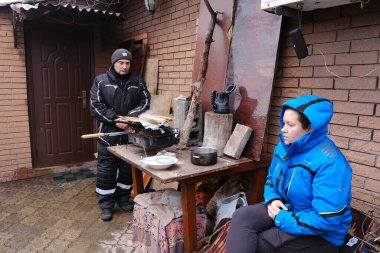 Mariupol, Ukrayna - 5 Mart 2022: Ailem Ukrayna 'nın Mariupol şehrinin bombardımanı altında bir şenlik ateşi etrafında ısınıyor ve yemek pişiriyor. Pencereler tahtalarla güçlendirilmiş. Telsiz masada..