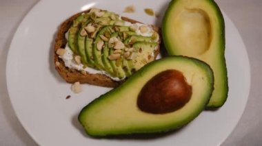 Avokado sandviçleri, beyaz bir arka planda yer fıstığı ve kabak tohumları ile ve bölünmüş avokado meyveleri