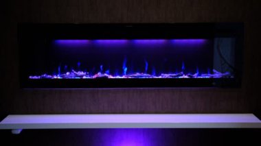 view on electric fireplace with artificial sparkling flame, decor for the interior, blue flame on crystals with violet purple backlighting.