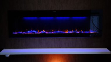 Elektrikli şömine üzerinde yapay parlayan alev, iç dekorasyon, kristallerde mavi ve turuncu arka ışıklandırmalı turuncu alev.