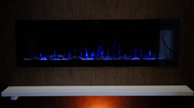 Elektrikli şömine, yapay parlayan alev, iç dekorasyon, kristallerin üzerinde turuncu arka ışıklandırmalı mavi alev..