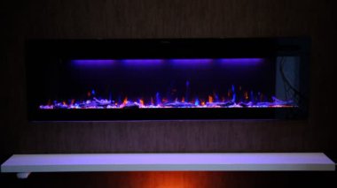 view on electric fireplace with artificial sparkling flame, decor for the interior, orange and blue flame on crystals with orange and purple backlighting