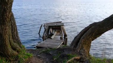 Autumn scene - lake and destroyed wooden pier. Old rotten wooden pier with missing planks with bench on a lake in the forest at autumn.