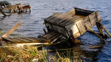 Autumn scene - lake and destroyed wooden pier. Old rotten wooden pier with missing planks with bench on a lake in the forest at autumn.