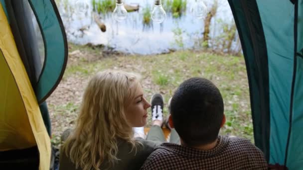 Widok z tyłu para siedzi w namiocie w pobliżu pięknej rzeki, jezioro. — Wideo stockowe