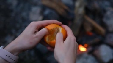 Kadın eli kabuğu soyulmuş tatlı mandalina, kamp yaparken ormanın şöminesinin üstüne yakın.