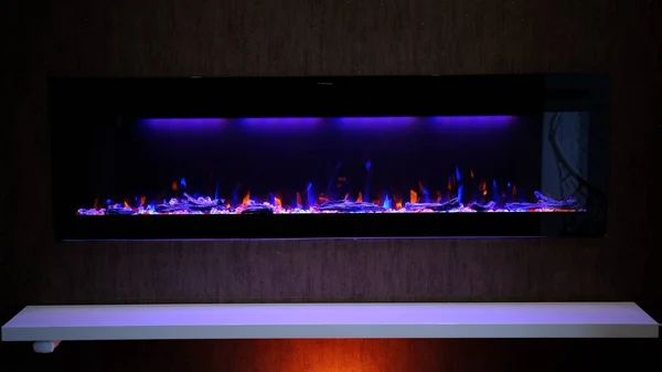 view on electric fireplace with artificial sparkling flame, decor for the interior, orange and blue flame on crystals with orange and purple backlighting