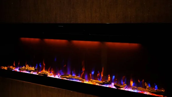Side view on electric fireplace with artificial sparkling flame, decor for the interior, blue and orange flame with suspended swing chair in reflection.