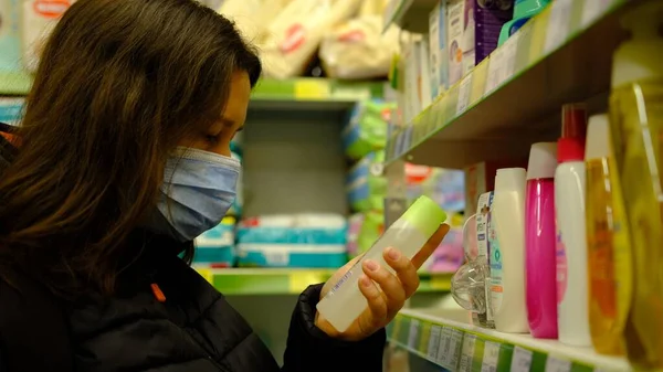 Woman choosing oil for massage, chemistry and self care products at a household goods in the store in mask.