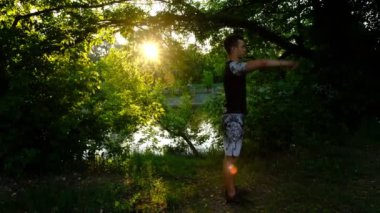 Tam boy yan görüş genç güçlü, sportif, atletik, formda spor elbiseli sporcu yaz günü nehrin kenarındaki parkta güneşin doğuşunda antrenman yapıyor.