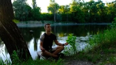 Parkta gölde çalışan yakışıklı, beyaz tenli genç adam, yarım Lotus, Padangustha Padma Utkatasana, elleri Namaste 'de, tam boy..
