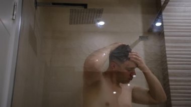 Adam duş alıyor, duş başlığından düşen suyun altında saç yıkıyor. Ev hayatı tarzında duş alan biri. Genç yetişkin vücut bakımı sabah rutini