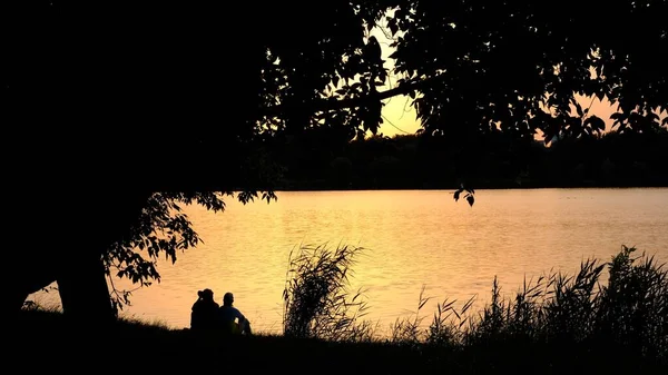 Silhouette of a couple in the afternoon behind a river couple in sunset on a lake.