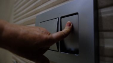 Yaşlı kadın tuvaletin sifonunu çekiyor, yaşlı kadın metal düğme kullanarak sifonu çekiyor..