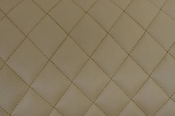 Background of beige leather quilted in the form of rhombuses.