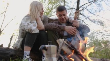 Slow motion 2x Closeup portrait of a couple sitting with guitar near bonfire in the forest.