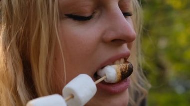 Slow motion 2x Woman with marshmallow by the fireplace. Young woman eating roasted marshmallow in the forest near the fireplace