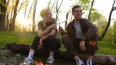 Slow motion 2x Camping and picnic concept. romantic couple frying marshmallow on fire in forest. Letters on soks mean RUSSIAN WARSHIP GO FUCK