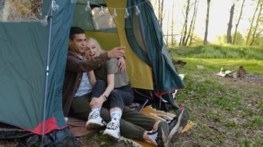 Haftasonu kamp çadırında dinlenen yavaş çekim genç çift. Erkek ve kız doğal manzaranın tadını çıkarıyorlar. Arkadaşlar birlikte dışarıda vakit geçiriyorlar.