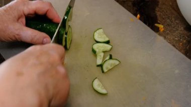 Sağlıklı beslenme, diyet konsepti. Mutfakta salatalık kesen yaşlı kadınların yüksek açı görüntüsü..
