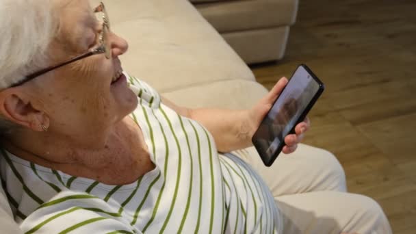 Ευχάριστη Ηλικιωμένη Κυρία Που Ξεκουράζεται Στον Καναπέ Χρησιμοποιώντας Εφαρμογές Smartphone — Αρχείο Βίντεο