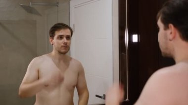 Young man examining his face while watching into the mirror.