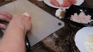 An old woman chops raw pork on a chopping board with a Knife.