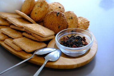 Dried tea leaves with tea pot and cookies on a gray table with spoons and wooden board.