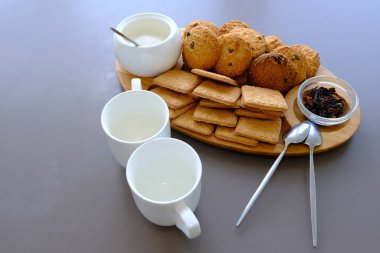 A tasty snack two cups of black tea and a plate of oatmeal cookies a wooden board on the gray background, leaf tea