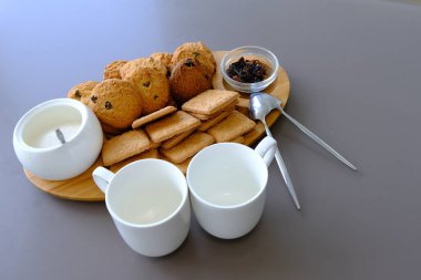 A tasty snack two cups of black tea and a plate of oatmeal cookies a wooden board on the gray background, leaf tea