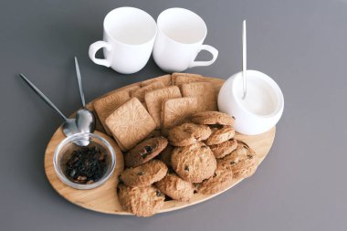 A tasty snack two cups of black tea and a plate of oatmeal cookies a wooden board on the gray background, leaf tea