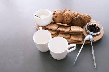 A tasty snack two cups of black tea and a plate of oatmeal cookies a wooden board on the gray background, leaf tea