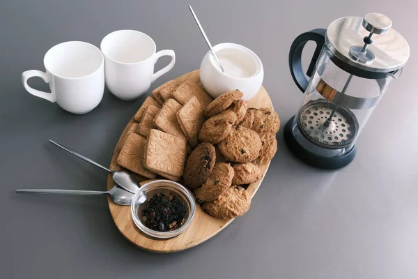 A tasty snack two cups of black tea and a plate of oatmeal cookies a wooden board on the gray background, leaf tea