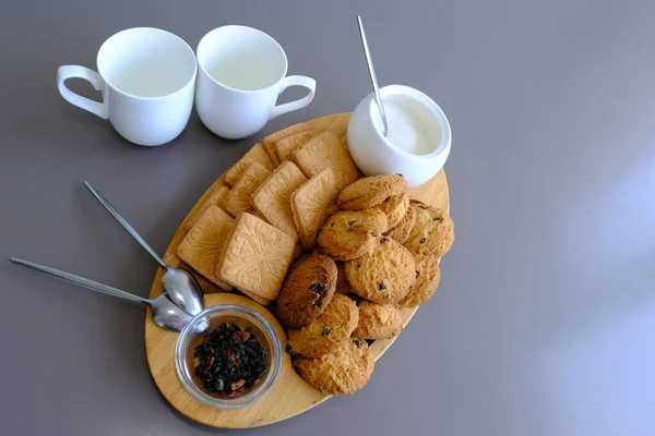 A tasty snack two cups of black tea and a plate of oatmeal cookies a wooden board on the gray background, leaf tea