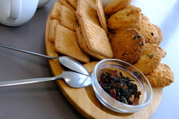 A tasty snack two cups of black tea and a plate of oatmeal cookies a wooden board on the gray background, leaf tea