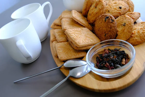 A tasty snack two cups of black tea and a plate of oatmeal cookies a wooden board on the gray background, leaf tea