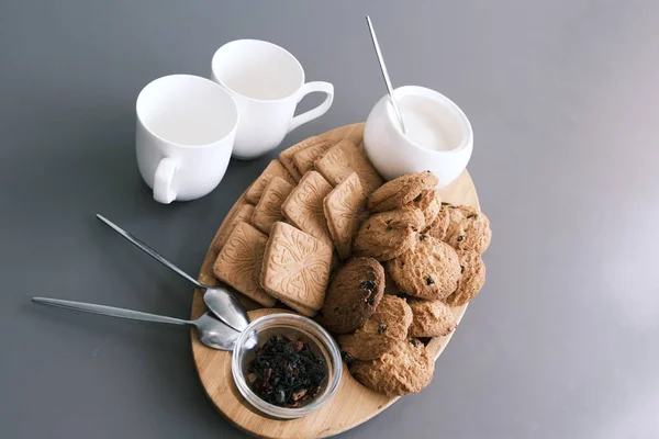 A tasty snack two cups of black tea and a plate of oatmeal cookies a wooden board on the gray background, leaf tea