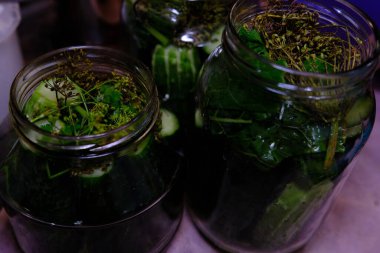 homemade canned cucumbers in big and small glass jars stand on kitchen table against.