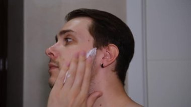 Close up of face of man applying foam on his chin with concentration.