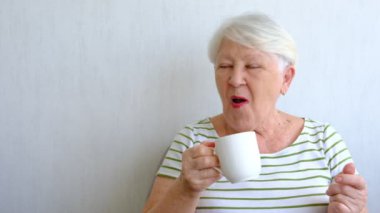 Smiling elderly woman enjoying time at home, drinking tea.