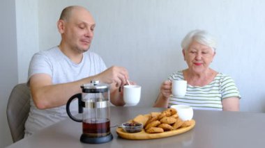 Hoş sohbet. Neşeli kadın kıdemli ve oturma odasında oturup, kahve içme ve Birbirinizle konuşmak genç oğlu.