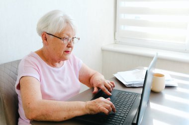 Financial problems. Disappointed senior lady reading document and talking to advisor by phone, working with documents and laptop.