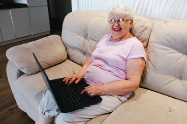 happy elderly woman using laptop computer at home. Senior mature older woman watching business training, online webinar on laptop computer remote working or social distance learning from home. 60s