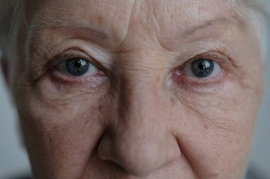 Close up portrait of beautiful older woman smiling and standing by wall with gray eyes.
