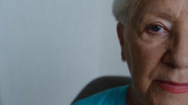 Close up portrait of beautiful older woman smiling and standing by wall with gray eyes.